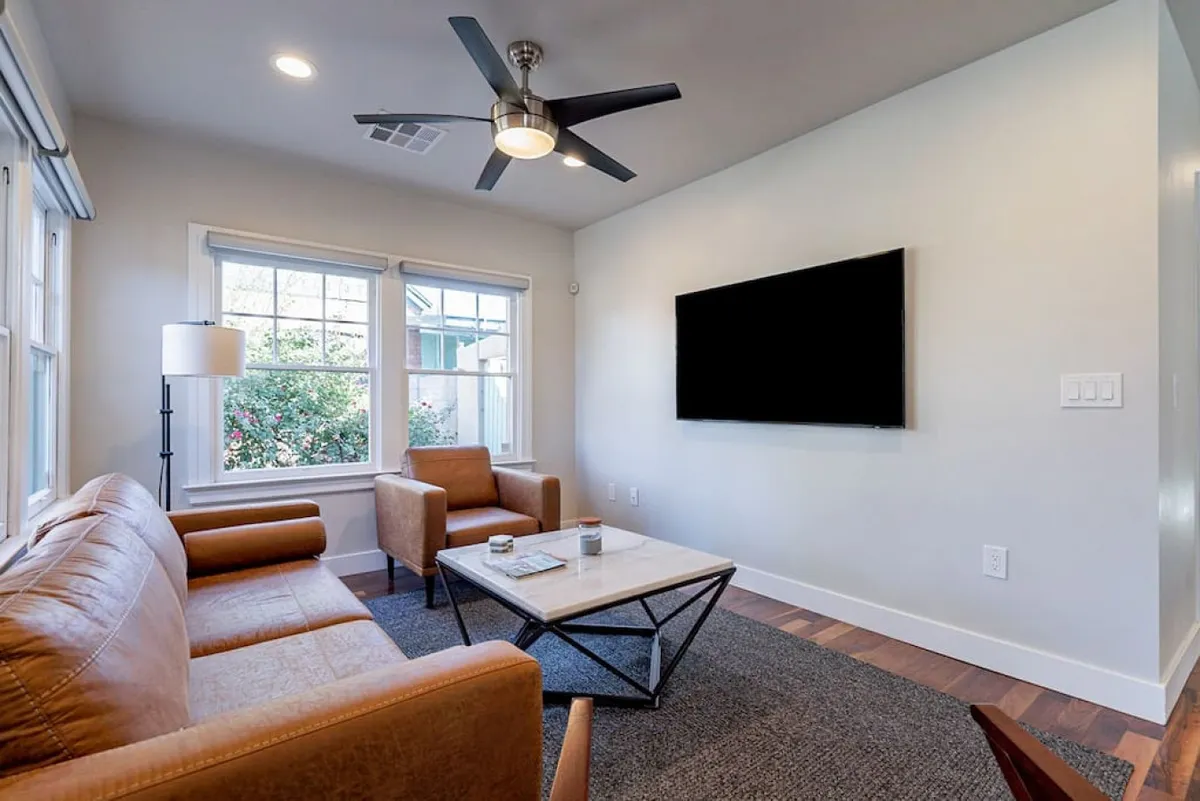 A cozy interior living space with a leather sofa, coffee table, and large windows letting in natural light. The room exudes comfort and warmth, suggesting a place to relax, share stories, or unwind after a night out.