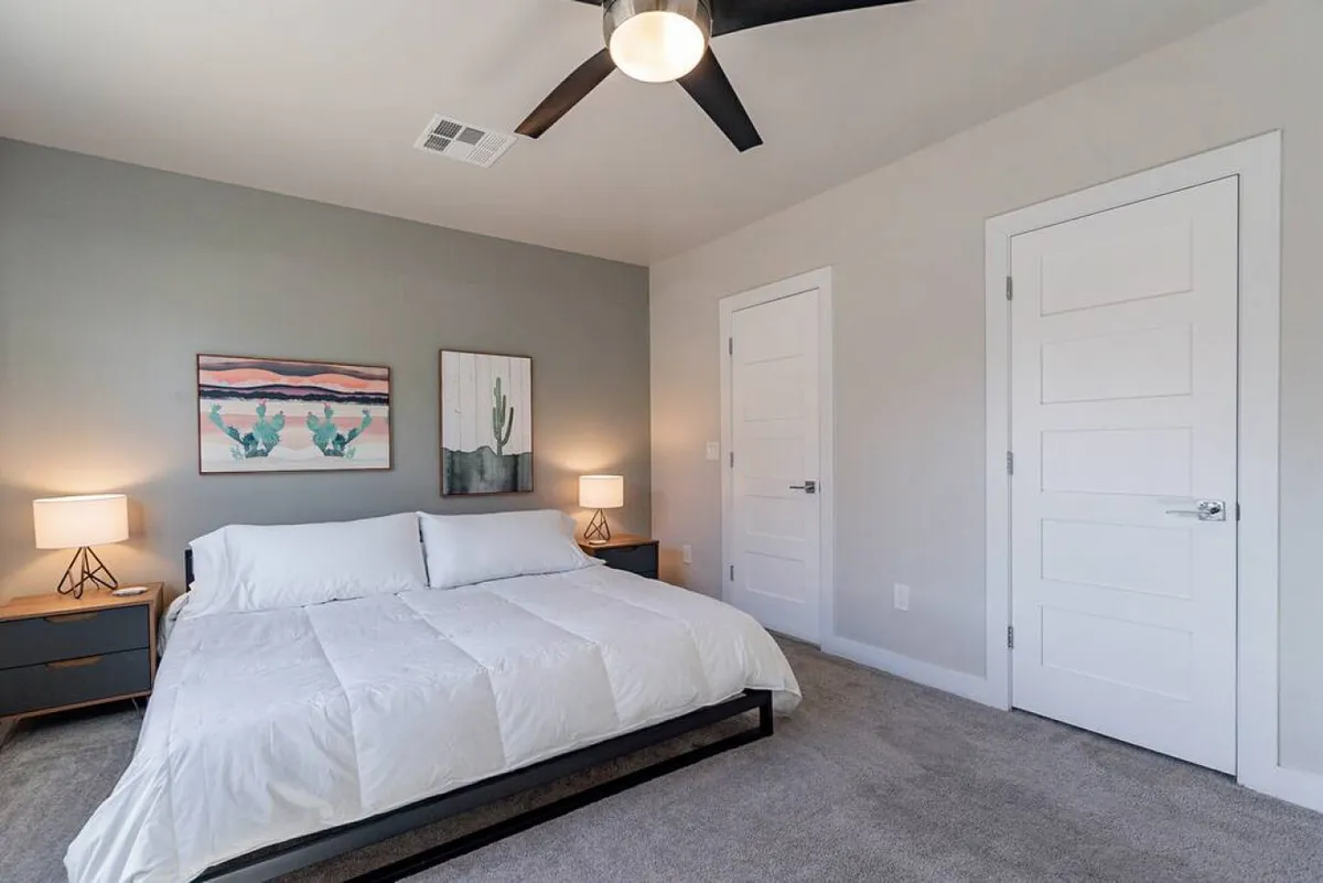 A serene bedroom featuring a comfortable bed with soft bedding, tasteful artwork on the walls, matching nightstands, and gentle lamp lighting. Natural light filters into the space, emphasizing its peaceful ambiance and the inviting textures of the linens.