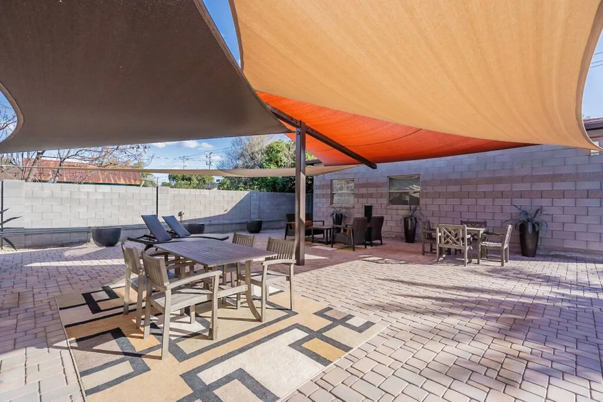 This image showcases an inviting outdoor dining area set under shade sails, with comfortable seating and decorative plants surrounding a spacious table. The area looks ideal for meals, group gatherings, or relaxed celebrations under the open sky.