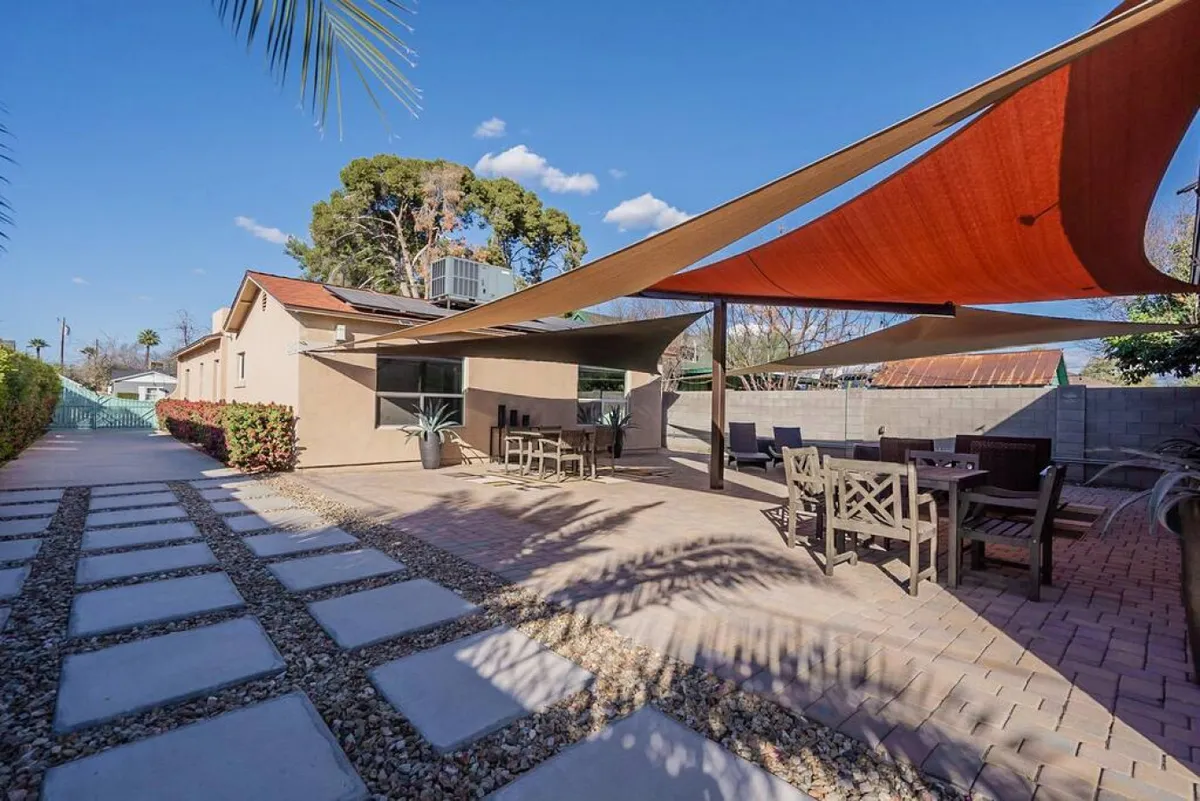An exterior shot of the outdoor seating area shaded by sails, with pathways and lush greenery, suggesting spaces for relaxation or informal gatherings just outside the property.