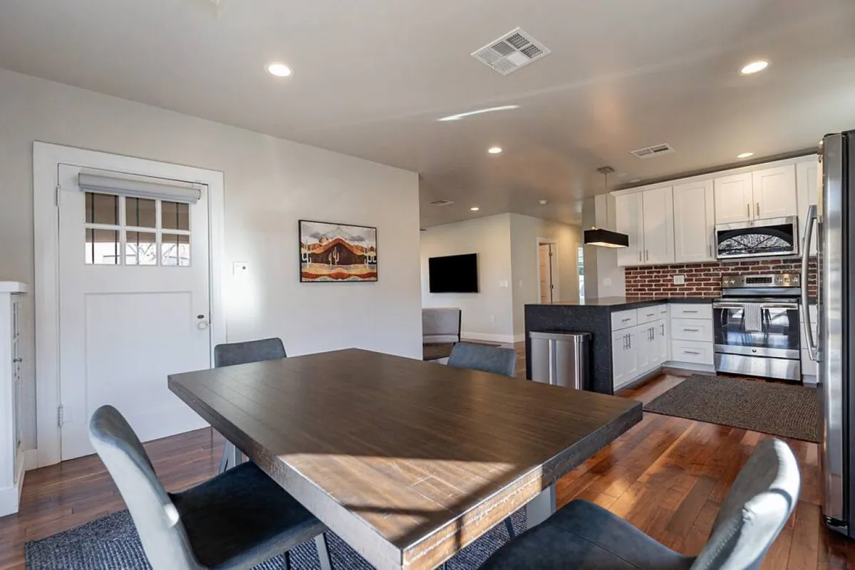 An open dining area seamlessly connected to the kitchen island, with a dining table, brick wall, and framed artwork. The space feels comfortable and welcoming, ideal for casual meals, family gatherings, or hosting friends.