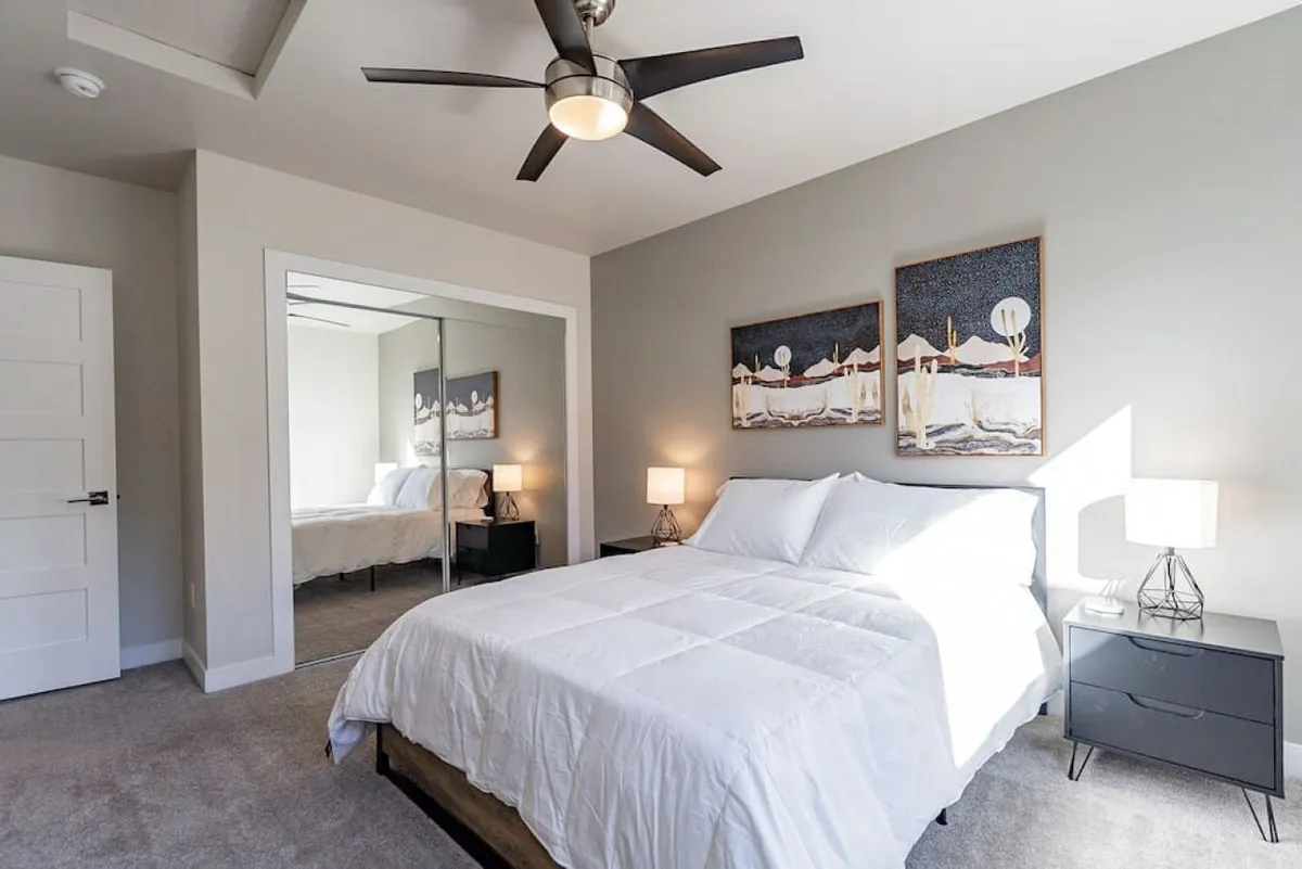 A tranquil bedroom with white bedding, modern artwork, and soft bedside lighting. The space is serene and inviting, perfect for restful nights or lazy mornings with a loved one.