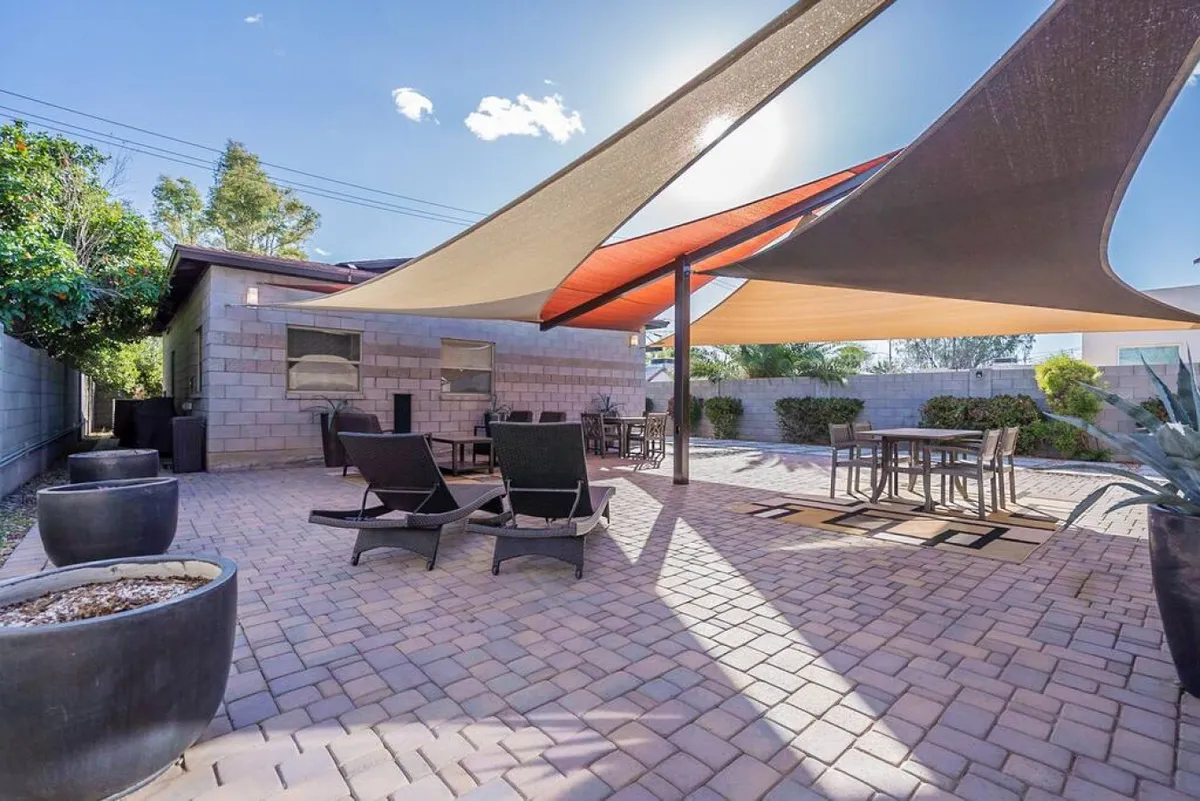 An inviting exterior patio shaded by canopies, featuring a dining table and comfortable seating surrounded by lush planters. The setting is ideal for outdoor dining, relaxing with a glass of wine, or enjoying a quiet moment together in a private, serene atmosphere.