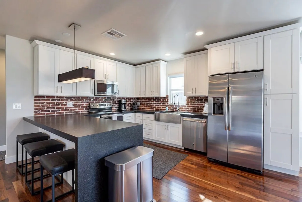 A stylish kitchen with a central island countertop, stainless steel appliances, and a brick backsplash. The scene is warm and inviting, showcasing ample space for cooking, gathering, and entertaining, while honoring the home's vintage roots with brick accents.