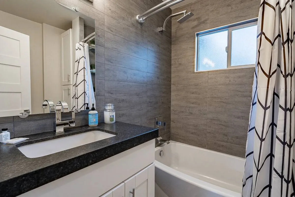 A bright, serene bathroom featuring a modern vanity with a sink, a relaxing bathtub with a shower curtain, a window letting in soft natural light, and soothing decor. The space feels inviting for both morning routines and evening relaxation.